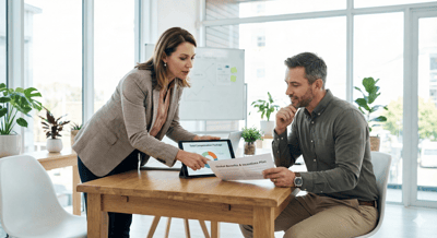 Directora de RRHH y ingeniero analizando su método de retribución gracias a un benchmarking salarial en una tablet con una planta industrial de fondo.